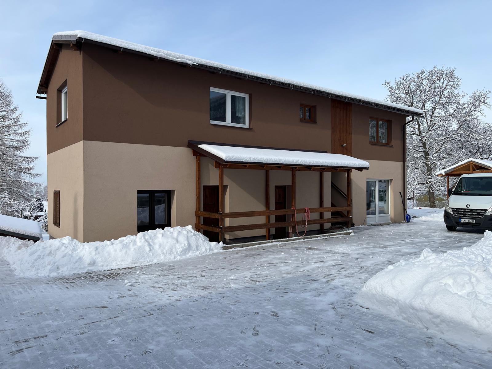 Dvoupatrová budova s apartmánem a krytým vstupem, kolem sníh a odhrnutý dvůr